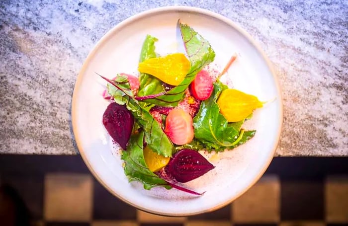 Seen from above, a dish of beets adorned with greens dangles from a countertop.