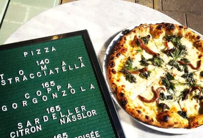 A full pizza beside a hand-written menu on a small marble table.