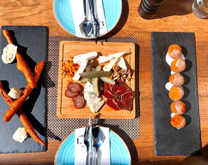 Viewed from above, a table adorned with a central plate of charcuterie and cheese, accompanied by breadsticks on one side and a fried appetizer on the other, complete with neatly arranged place settings.