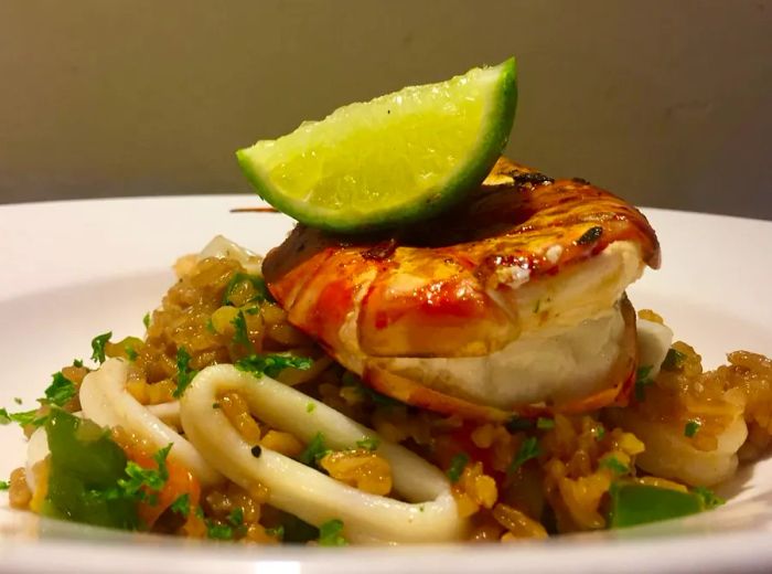 A sizable broiled shrimp rests atop a generous serving of rice and rings of squid, crowned with a lime wedge perched on top.