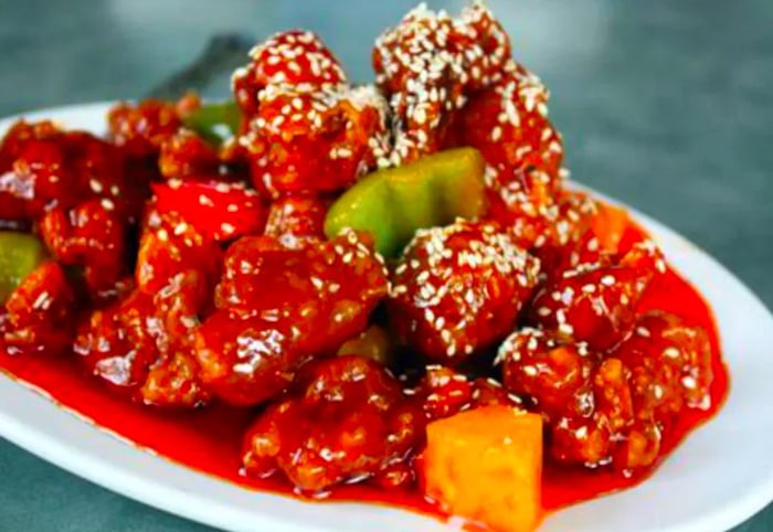 Tender pieces of pork coated in a thick sauce, served alongside diced peppers and pineapple, all sprinkled with sesame seeds on a plate.