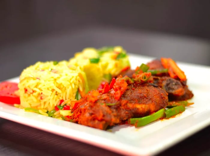 Chunks of meat smothered in a rich sauce accompany a mound of rice and a medley of vegetables on a large white plate.