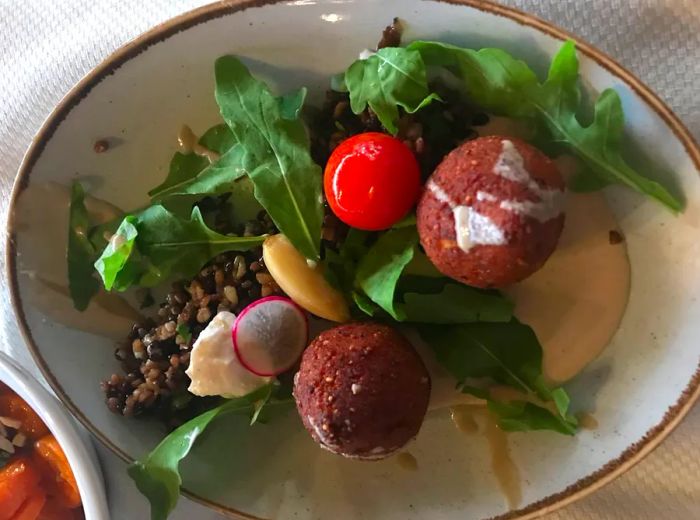 An aerial view of a plate filled with kubbeh (croquettes) accompanied by a fresh salad, resting on a white dish atop a patterned tablecloth