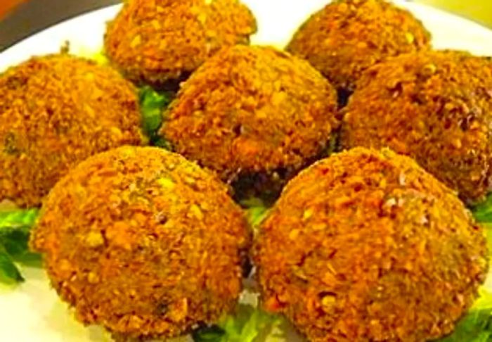 A small plate features six falafel balls resting atop a bed of fresh greens.