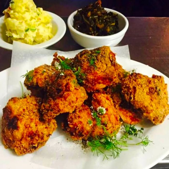 Chunks of fried chicken are served on butcher paper alongside diced herbs, with small bowls of potato salad and vegetables complementing the dish