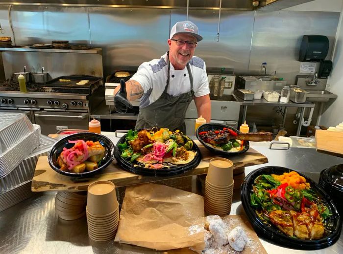 Chef Wes Stepp stands in his kitchen, showcasing meals packed in plastic containers.