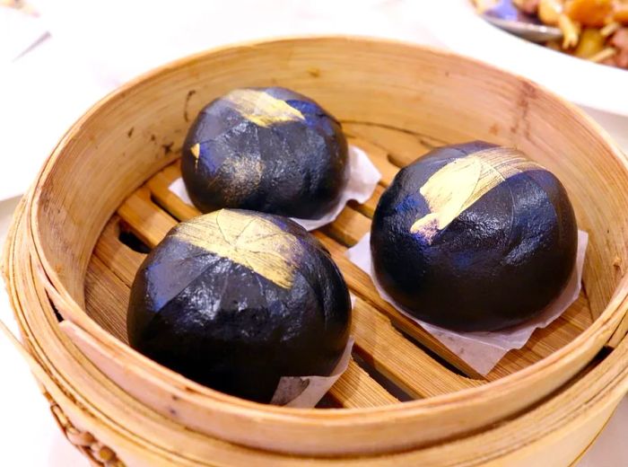 A steamer basket holds three large, glossy black steamed buns, ready to be enjoyed.