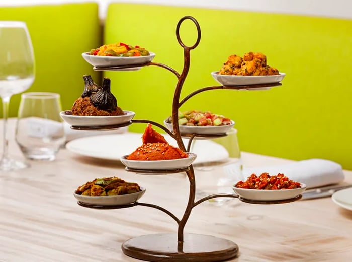 A beautifully crafted metal sculpture resembling a tree holds an array of dishes on its branches, elegantly displayed on a table set for dining.