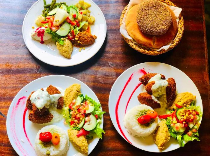 An aerial view of a wooden table displaying a variety of dishes, including flatbreads, different types of falafel, and fresh vegetables.