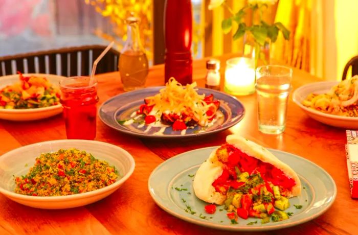 A candlelit table adorned with various ceramic plates, showcasing dishes like a grain salad and a pita sandwich, creating a warm dining atmosphere.