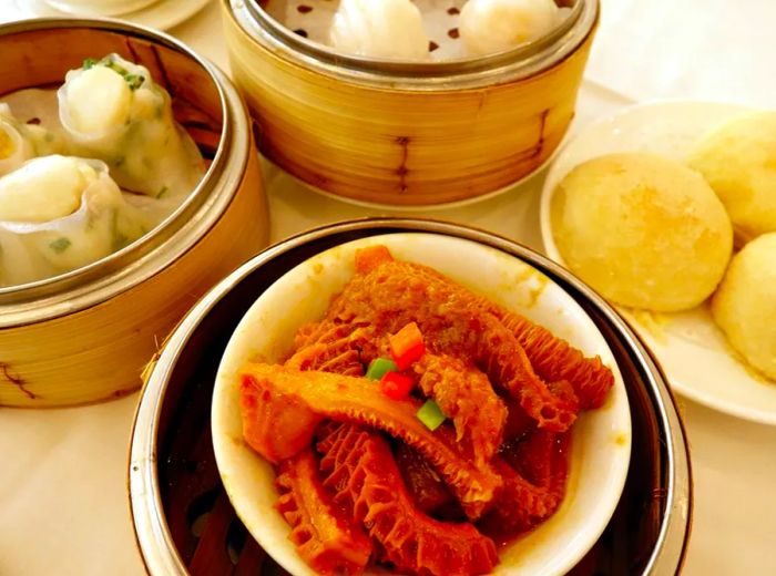 A table displaying steamer baskets filled with dumplings, accompanied by a plate of steam buns and another plate of tripe.