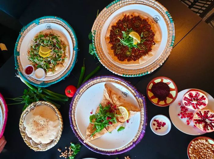 Aerial view of a dark table adorned with various decorative plates, each showcasing flatbreads topped with an assortment of ingredients, alongside dips and sides.