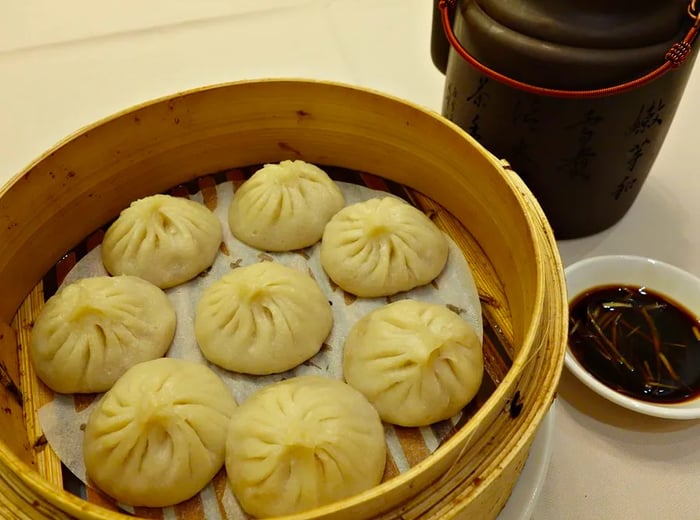 A steamer basket brimming with flavorful soup dumplings, accompanied by a small dish of dipping sauce.