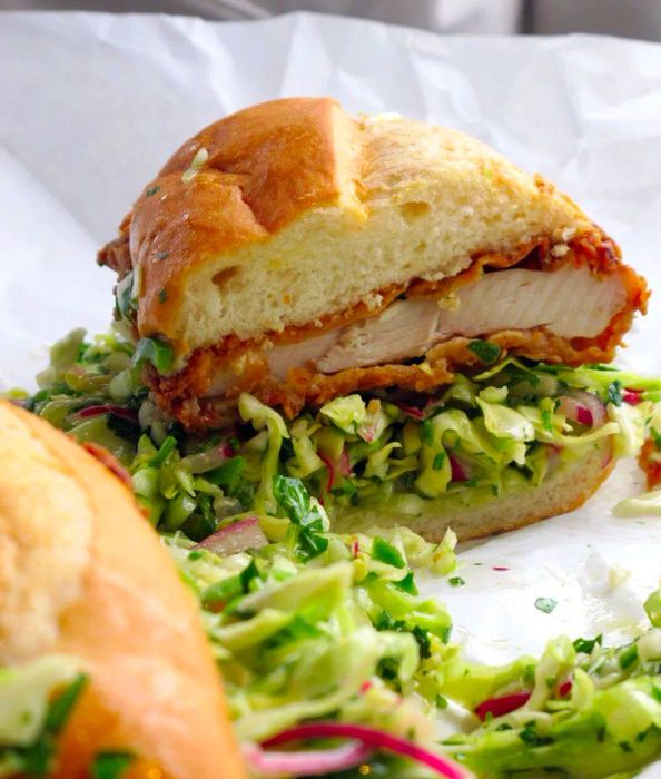 A fried chicken sandwich sliced in half, with lettuce overflowing