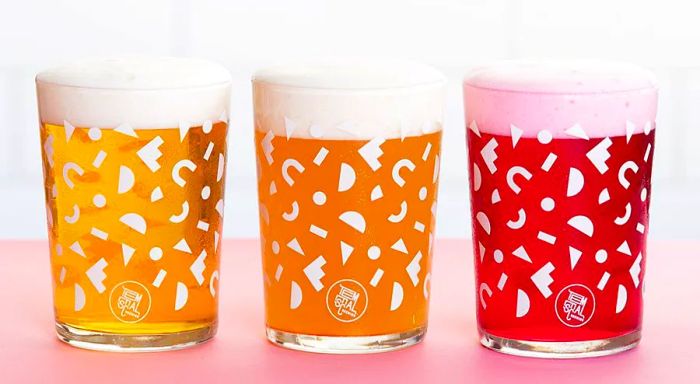 Three glasses of beer, each in different hues, sit next to one another in stylish glasses