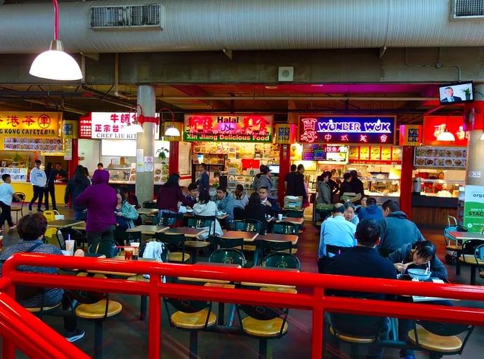 Food court tables are filled with diners enjoying meals from various vendors in a spacious mall setting.