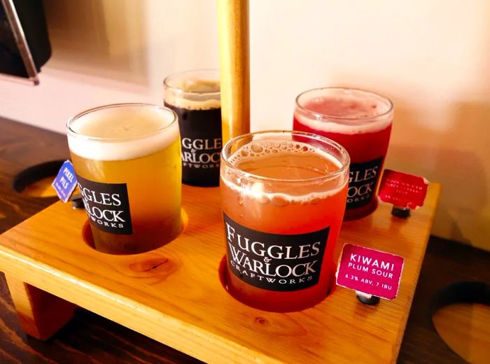 Four full beer glasses arranged in a wooden tray, each labeled with a small tag nearby.