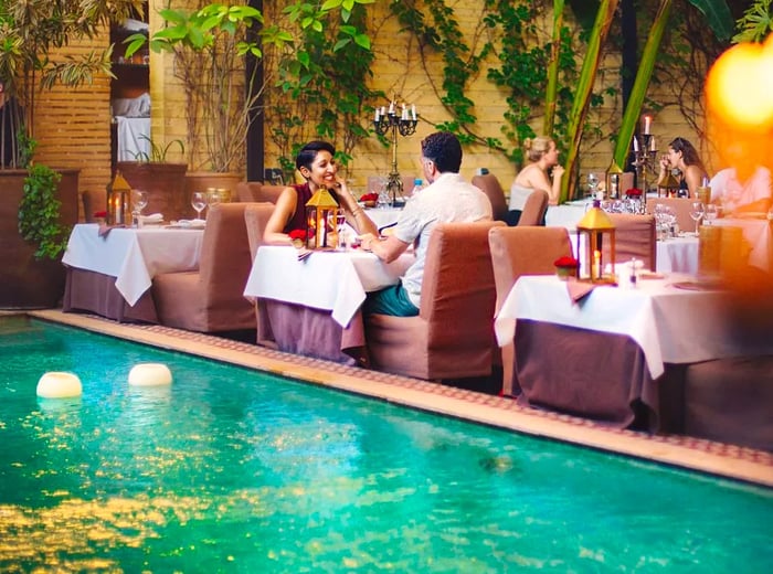 Patrons are seated at various tables set around a pool, surrounded by lush greenery.