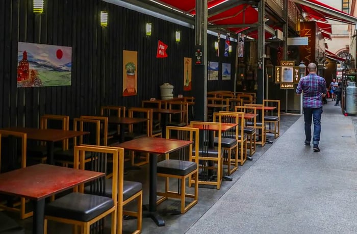 A server passes by rows of vacant tables and chairs