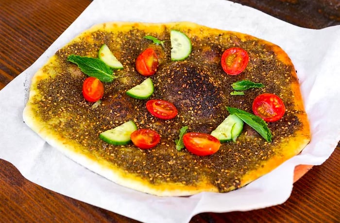 Aerial view of flatbread topped with spiced ground beef, herbs, and sliced vegetables on wax paper