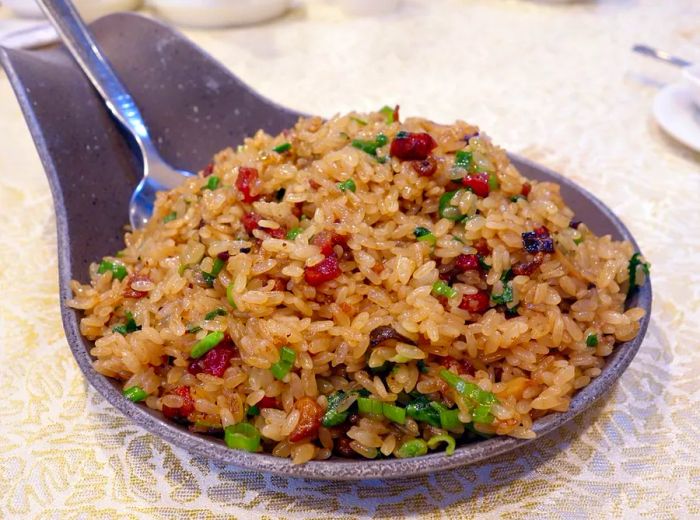 A generous spoon-shaped dish brimming with fried rice, dotted with meat and vegetables, with a spoon nestled at one end.