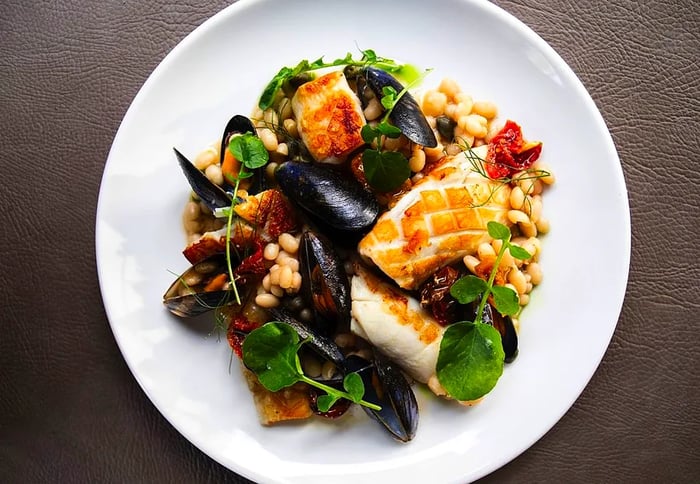 A plate features an array of mussels, grilled fish, fresh greens, and other delightful accompaniments.