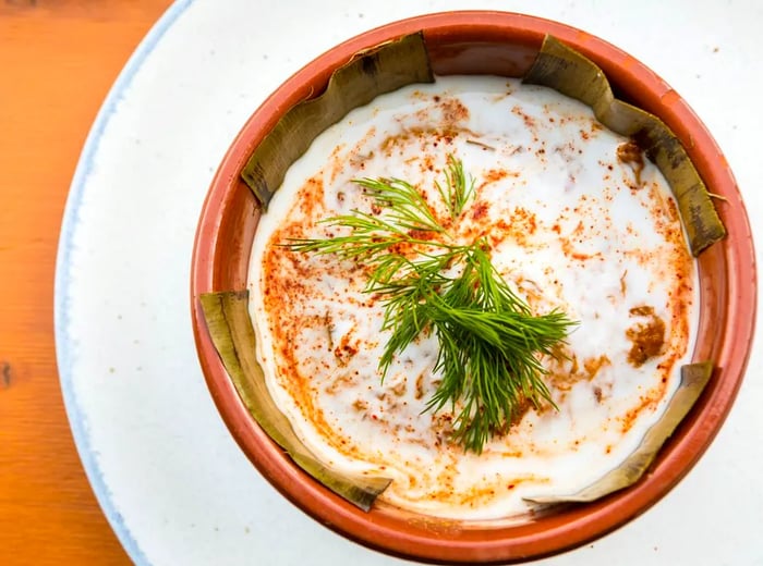 A bird's-eye view of a clay bowl filled with a thick layer of spice-infused custard and garnished with chopped herbs, resting on a white plate atop a wooden table