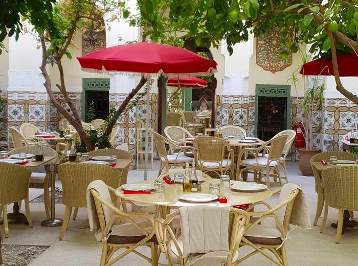 An unoccupied courtyard with expansive trees casting shade over arranged patio tables.