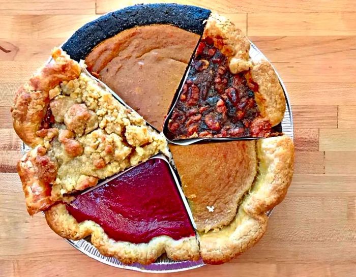 An overhead view of a whole pie composed of slices from five different flavors, each topped with unique crusts and crumbles