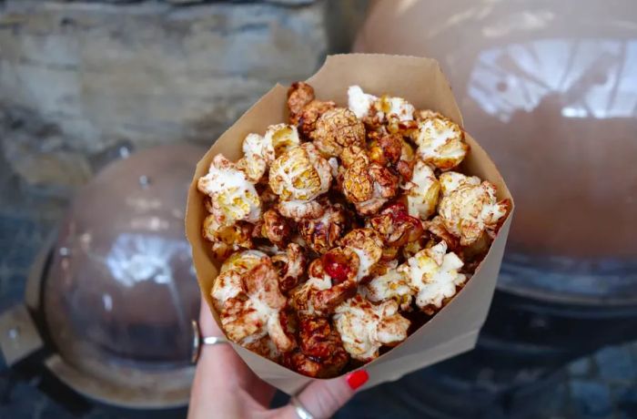 A hand grips a paper cone filled with chocolate-covered popcorn