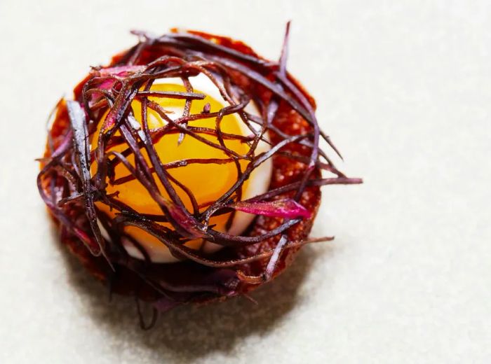 A soft-boiled egg rests in a delicate red nest on a pristine white plate.