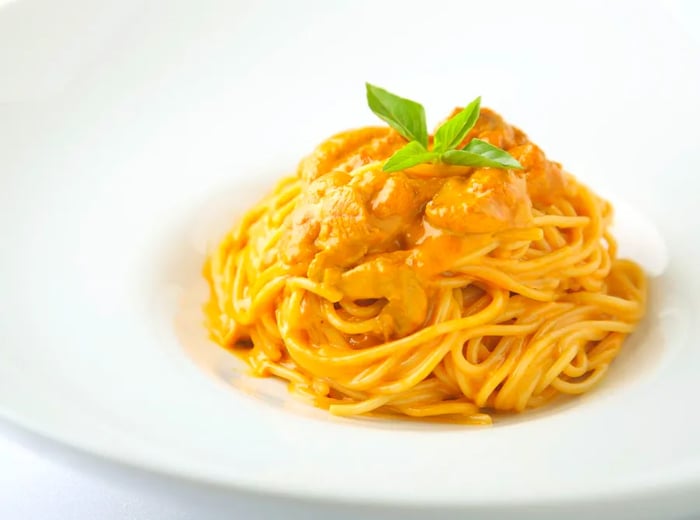 A serving of spaghetti topped with rich sea urchin sauce and garnished with a small basil leaf.