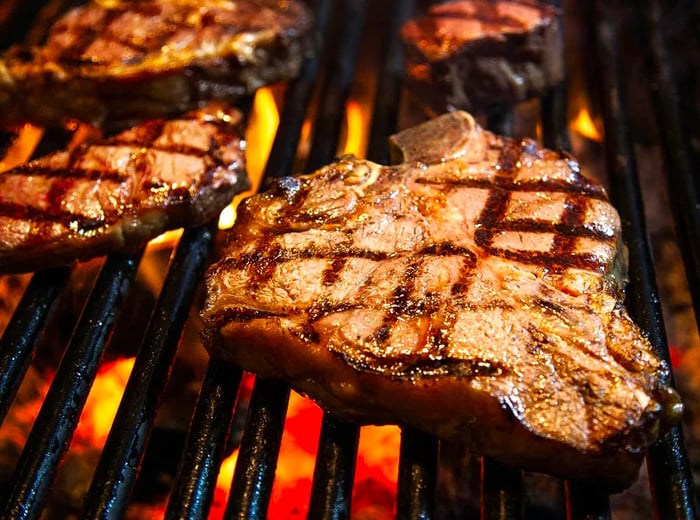 Juicy, thick-cut steaks with charred grill marks resting over an open flame.