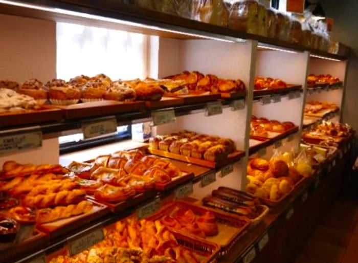 Shelves filled with an array of pastries and loaves of bread in front of a large window