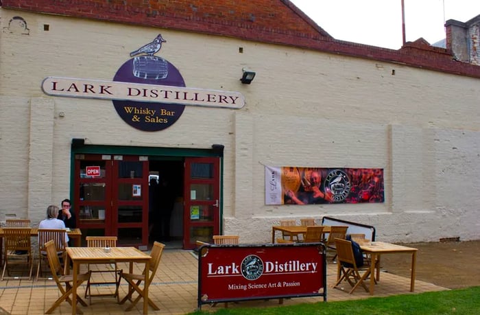 The facade features a white brick window adorned with a prominent Lark distillery logo, complete with an illustration of a bird above the entrance doors.