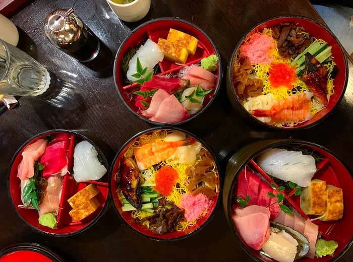 An overhead view of a table showcasing various bowls filled with sliced fish over rice and separate ingredients, elegantly arranged.