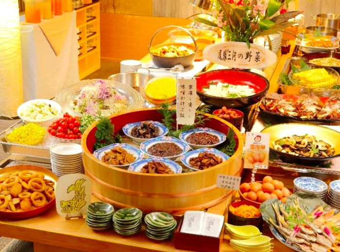 A buffet spread brimming with steamer boxes, vibrant ceramic dishes, and platters filled with an assortment of Japanese delicacies, including fish, fried items, and vegetables.