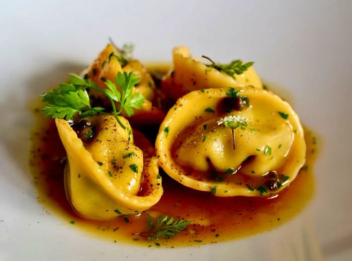 Four generously filled tortellini rest in a small pool of sauce, elegantly garnished with herbs.