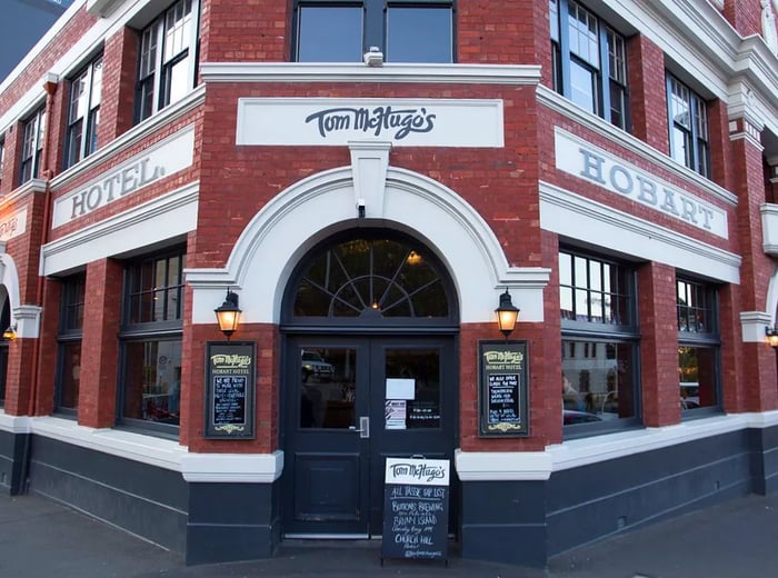 The exterior of Tom McHugo’s features a grand entrance with the restaurant's name elegantly scripted above, set against a sizable red brick building at a bustling street corner.