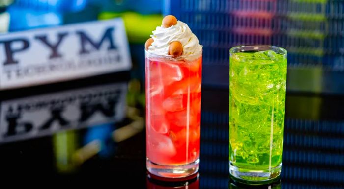 Two vibrant drinks in highball glasses, one adorned with whipped cream and accompanied by small snacks.