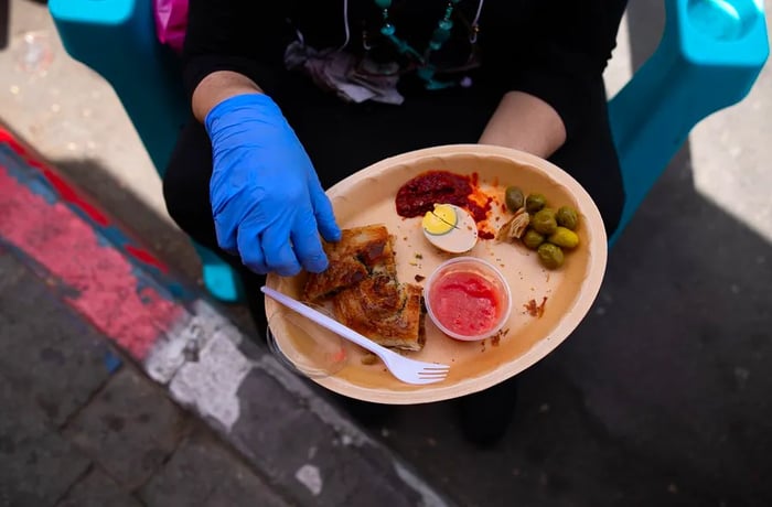 A woman carefully eats a dish from Levinsky Burekas while seated on a plastic chair in a section of Levinsky market that has been transformed into a pedestrian area in Tel Aviv, Israel, on June 2, 2020.