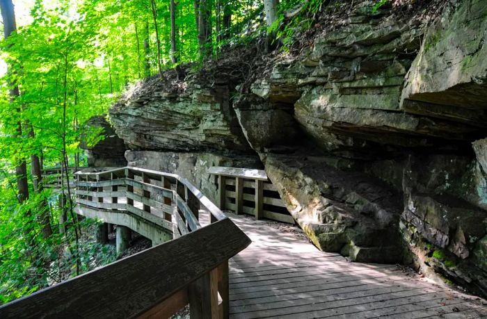 A wooden bridge set against towering cliffs and lush greenery.