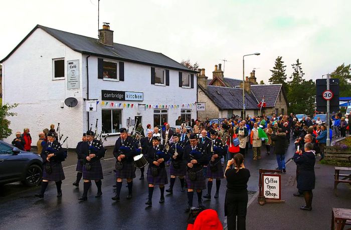 A procession of bagpipers winds through a historic Scottish village.