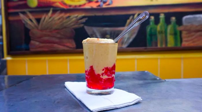 A glass filled with red gelatin and ice cream, resting on a napkin with a spoon beside it.