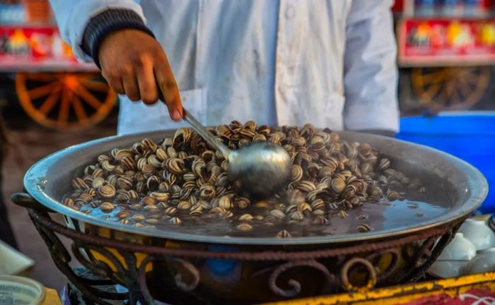 A large ladle stirs a bowl of snail soup.