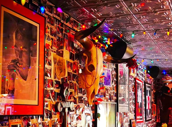 A decorative animal skull adorns a bar wall filled with Polaroid snapshots, string lights, and eclectic decorations.