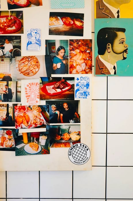 A close-up of a vibrant assortment of photographs and illustrations depicting people and food, all pinned to a white tiled wall inside Gumbo Yaya.