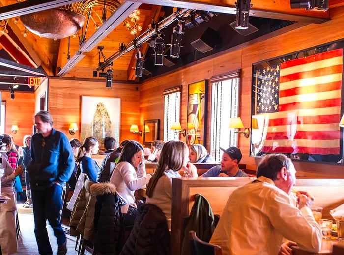 Diners enjoy their meals in a restaurant adorned with wooden walls and large American Flag artwork.