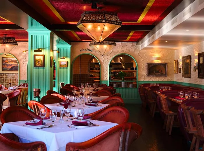 An exterior view of the restaurant featuring white and teal colors, arched doorways, tiled walls, and prominent pendant lighting.