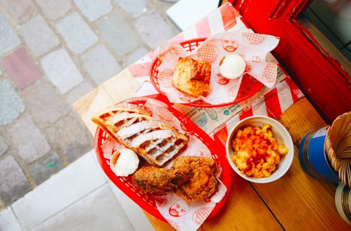 Red plastic baskets filled with Gumbo Yaya’s fried chicken and waffles, along with a biscuit and a bowl of macaroni and cheese, rest on a wooden counter in the restaurant.